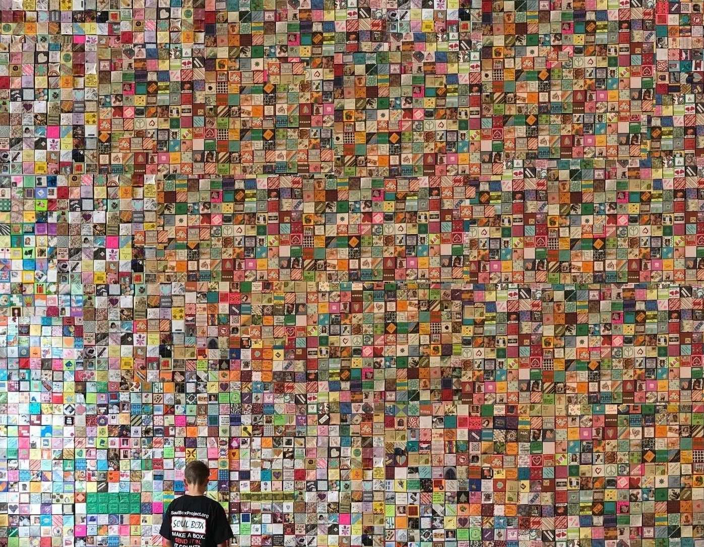 Boy looks at wall of Soul Boxes representing one month of deaths